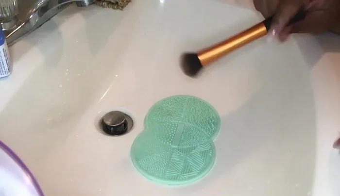 Scrub the brush using small circular motions on the mat's different sections. Rinse and repeat 2-3 times for foundation brushes.