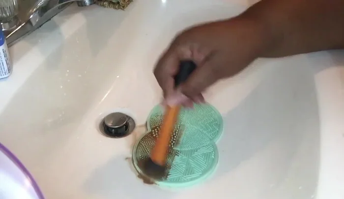 Scrub the brush using small circular motions on the mat's different sections. Rinse and repeat 2-3 times for foundation brushes.