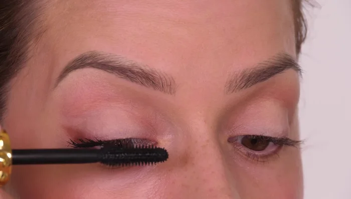 Apply mascara, looking down into a mirror to avoid smudging on the lid. Curl lashes with a curler, focusing on the outer third for a lifted effect.